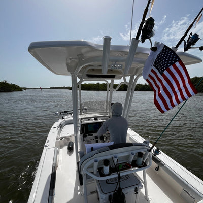 Customer's center-console fishing boat with an American flag strapped to the T-top beside the rod holders, angler at the helm.