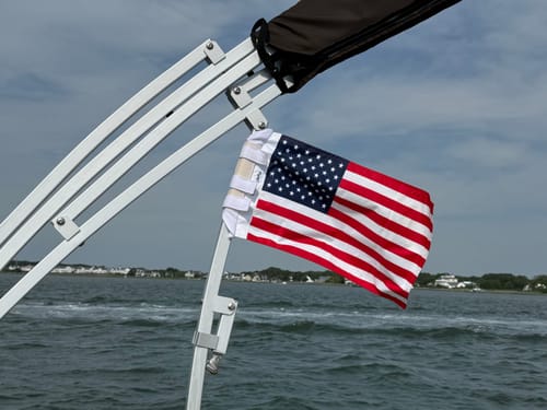 Customer's American Flag attached to a boat frame, waving over the water on a bright day.