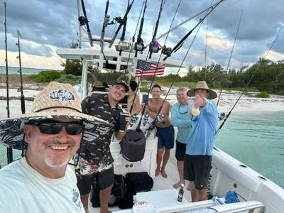 Six friends raising drinks on the deck of a center console beached on a sandbar, an American flag strapped to the T-top