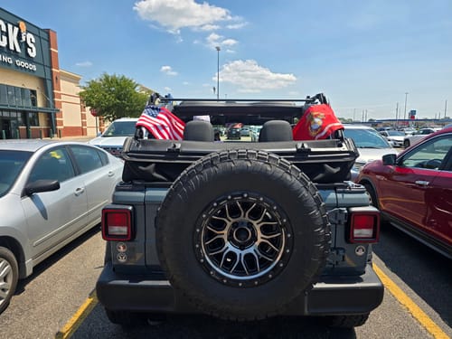 American flag attached to the back of a parked Jeep in a sunny parking lot.