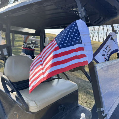 American Flag strapped to the rear roof post of a golf cart on the course, Happy Hour flag behind it.