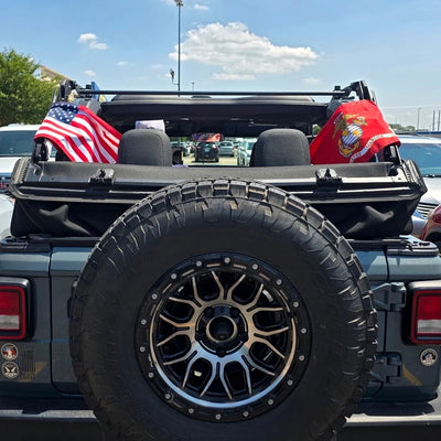 A customer's American flag and Marine Corps flag strapped to the roll bar of an open-top Jeep, seen from behind.