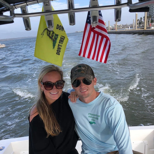 A couple sitting at the stern of a boat under a Gadsden flag and an American flag strapped to the rocket launcher