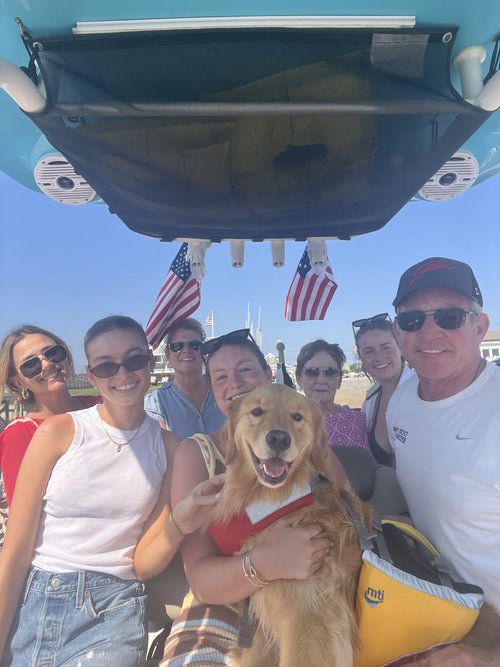 A family crowded onto a boat with their golden retriever, two American flags strapped to the T-top above them