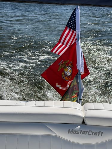 Customer's United States Marine Corps flag and a US flag mounted to the back of a white MasterCraft boat on the water.