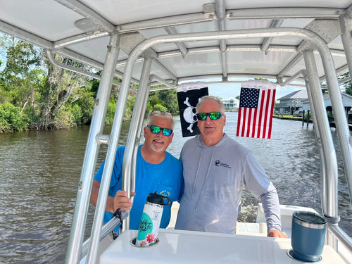 Two men at the helm of a center console under a Jolly Roger and an American flag strapped to the T-top