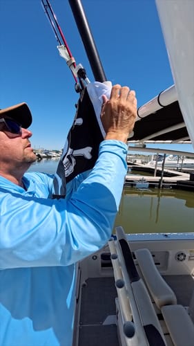 Customer attaching a black Jolly Roger Flag to a pole on a boat in a marina.