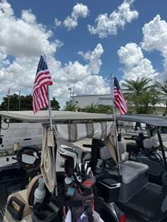 Two American Flags mounted on poles on the back of a golf cart.