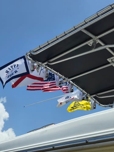 United States Army Flag and other flags displayed on a boat top under a clear blue sky.
