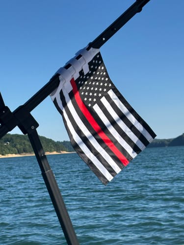 A customer's Thin Red Line Flag flying from a black bar on a boat over blue water.