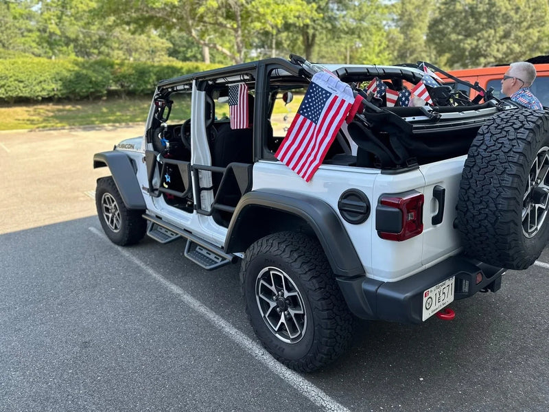 American flags strapped to the roll bar of a white Jeep Wrangler Rubicon with its top off