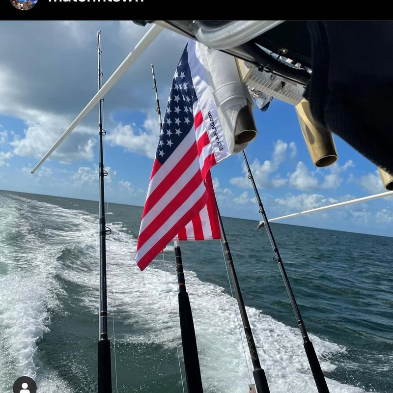 An American flag strapped to a rod holder on a center console running offshore, wake and rods in frame